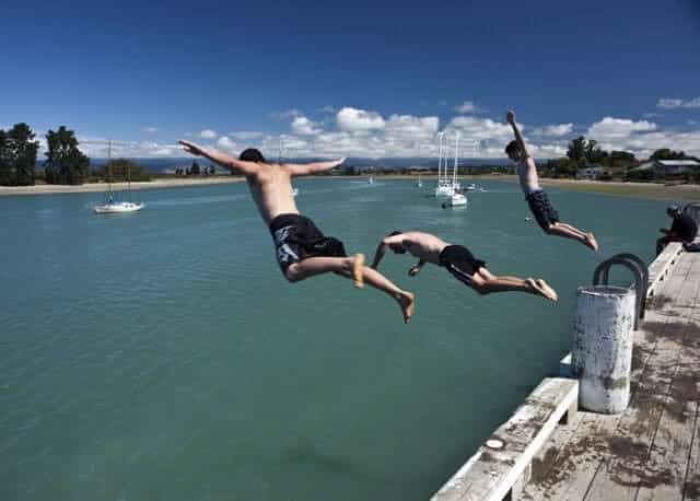 Image of three lads jumping into the water from the pier in Mapua