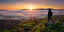 Mobile menu image of a male stood on a rock at the top of a mountain overlooking a landscape covered in cloud