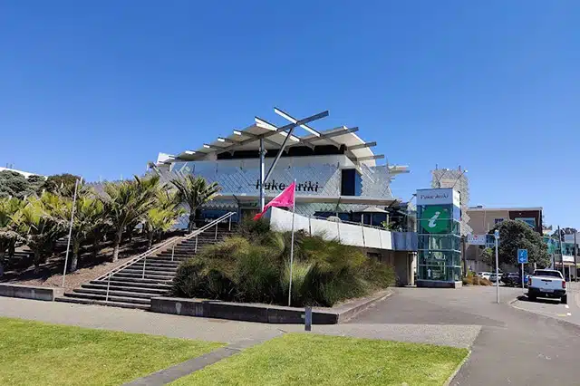 A pink flag next to the lawn at the bottom of some stairs leading up to an artistically designed grey building 