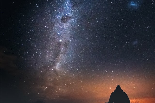 silhouette of man sitting and watching the stars 