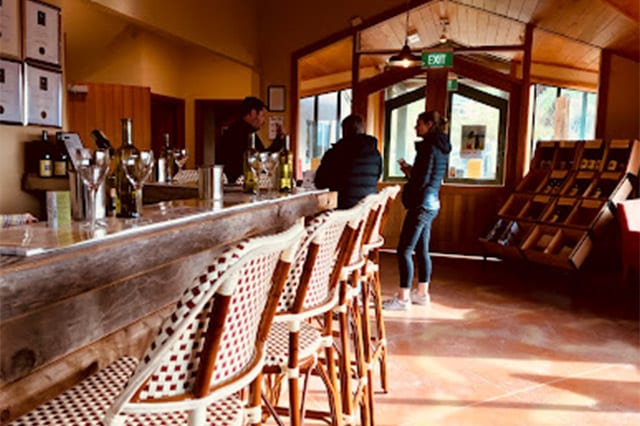 two people speaking with the bar tender at the bar inside the winery