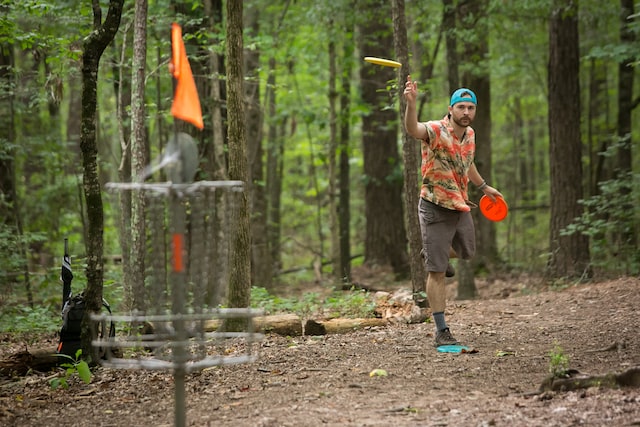 man in colourful shirt and blue cap throwing yellow frisbee towards a net