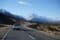 White car driving on left-hand side of the road in new zealand with mountain landscape background