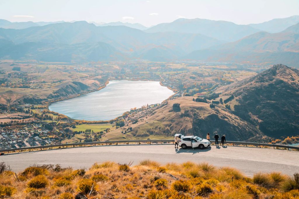 A group of friends standing outside their GO Rentals vehicle overlooking new zealand queenstown landscape