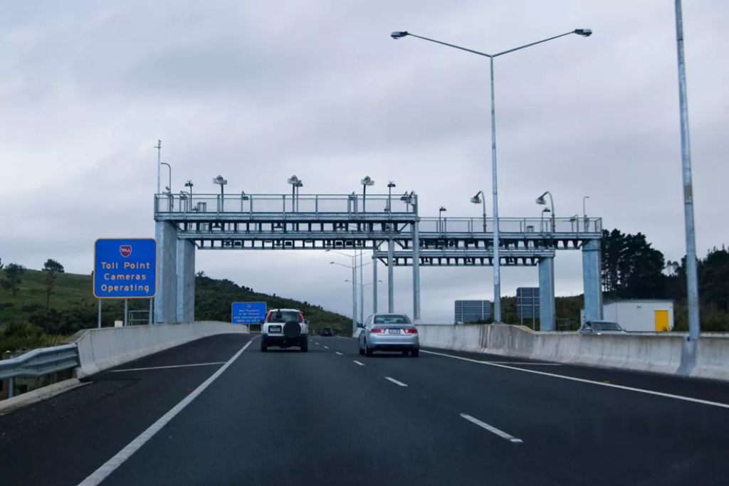 driving on road with two cars in front and a toll road sign