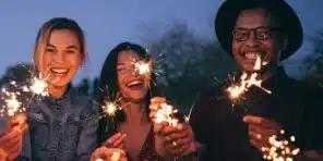 Group of friends smiling and holding sparklers at night during a celebration
