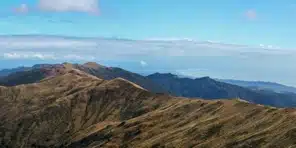 Panoramic view of golden mountain ridges under a blue sky with the ocean in the distance